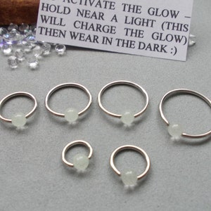Puede incluir: Una colecci&oacute;n de aros para la nariz de color plateado con una peque&ntilde;a cuenta redonda y brillante. Los aros var&iacute;an en tama&ntilde;o y est&aacute;n dispuestos sobre una superficie gris. En el fondo se ve una peque&ntilde;a tarjeta con instrucciones.