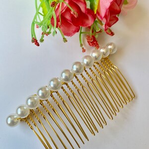 May include: A gold hair comb with a row of white pearl beads. The comb has a twisted design and is made of metal.