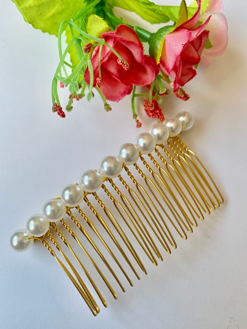 May include: A gold hair comb with a row of white pearl beads. The comb has a twisted design and is made of metal.
