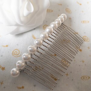 May include: A silver hair comb with a row of white pearl beads.