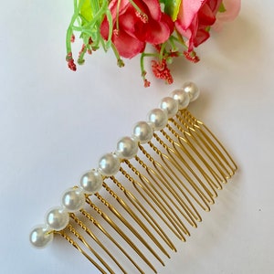 May include: A gold hair comb with a row of white pearl beads. The comb has a twisted design and is perfect for adding a touch of elegance to any hairstyle.