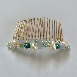 Può includere: Un pettine per capelli dorato decorato con perle e perline bianche e blu. Il pettine presenta una varietà di forme e dimensioni di perle e perline.