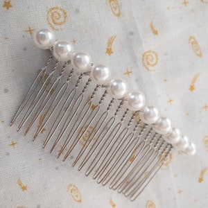 May include: A silver hair comb with a row of white pearl beads.