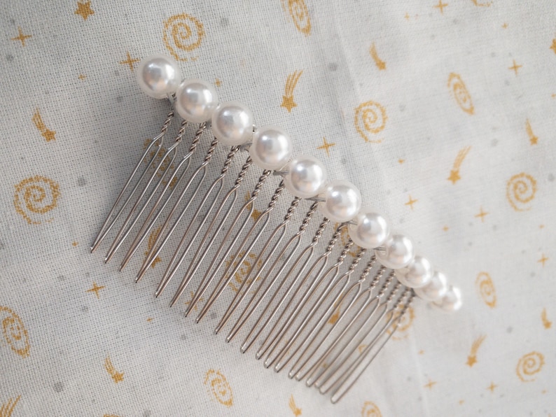 May include: A silver hair comb with a row of white pearl beads.