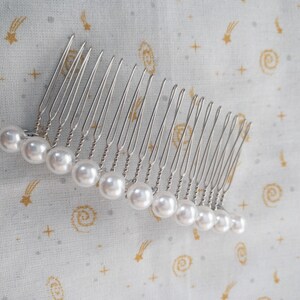 May include: A silver hair comb with a row of white pearl beads attached to the teeth.