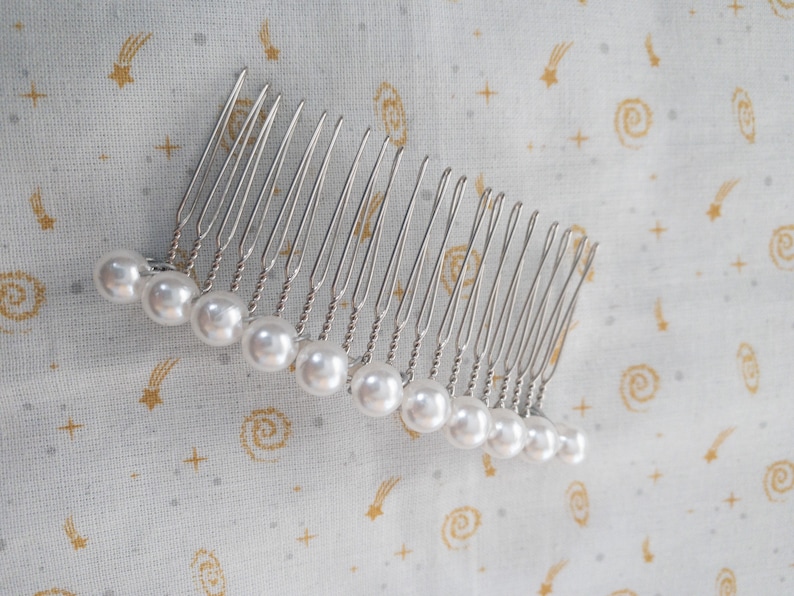 May include: A silver hair comb with a row of white pearl beads attached to the teeth.