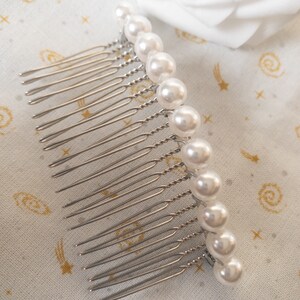 May include: A silver hair comb with a row of white pearl beads. The comb has a twisted wire design and is perfect for adding a touch of elegance to any hairstyle.