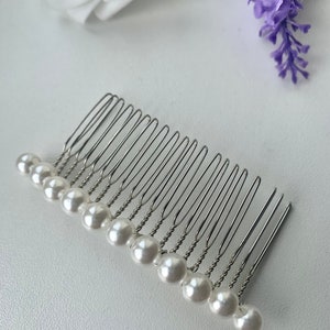 May include: A silver hair comb with a row of white pearl beads attached to the teeth.