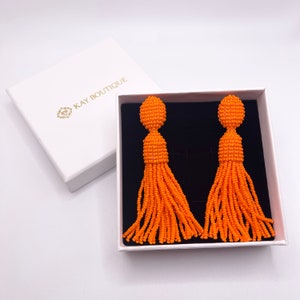 May include: A pair of orange beaded tassel earrings in a white box with the text "KAY BOUTIQUE".