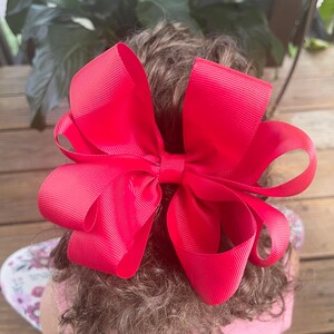 May include: A large, bright pink hair bow made of grosgrain ribbon. The bow is tied in a classic style with two loops and a center knot.