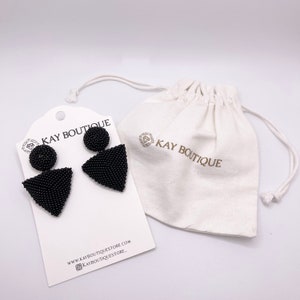 May include: Black beaded earrings with a round top and a triangular bottom. The earrings are displayed on a white card with the text "KAY BOUTIQUE" and website information. The earrings are packaged in a white drawstring bag with the text "KAY BOUTIQUE".
