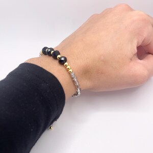 Könnte beinhalten: Ein Armband aus schwarzen und goldenen Perlen mit einer silbernen Kette. Das Armband besteht aus schwarzen facettierten Perlen, goldenen Perlen und einer silbernen Kette.