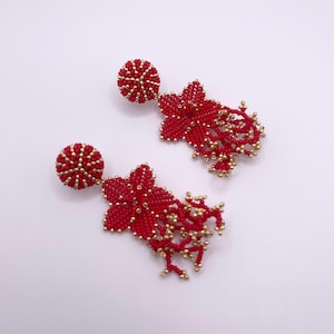 Op de afbeelding: Een paar rode kralen oorbellen met gouden accenten. De oorbellen hebben een stervormig ontwerp met een hangende kwast.