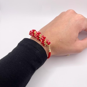 May include: Red and gold beaded bracelet with a red cord closure.
