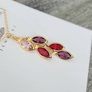 May include: Gold chain necklace with a pendant of five marquise-shaped gemstones. The gemstones are pink, red, and purple.