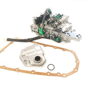 May include: A silver automotive transmission valve body with a black wire harness, a silver transmission filter, a brown gasket, and a black o-ring.