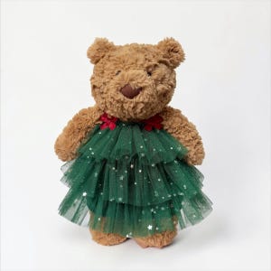Könnte beinhalten: Ein brauner Plüschteddybär mit einer strukturierten, flauschigen Oberfläche. Der Bär trägt einen mehrlagigen, dunkelgrünen Tüllrock, der mit kleinen, silbernen sternförmigen Pailletten und zwei kleinen roten Stoffschleifen am Ausschnitt verziert ist.