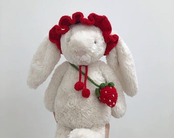 May include: White plush bunny with a red crocheted flower hat and a green and red crocheted strawberry hanging from its neck.