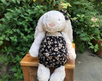 May include: A white plush bunny rabbit wearing a black and white floral dress with a white lace trim. The bunny is sitting on a wooden stool.