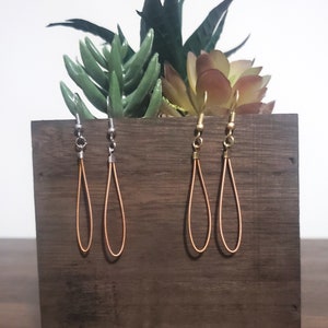May include: Four pairs of dangle earrings with copper wire loops and silver or gold hooks. The earrings are displayed on a wooden surface.