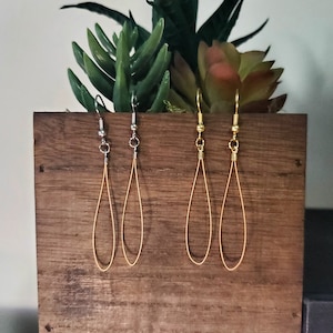 May include: Four pairs of dangle earrings displayed on a wooden board. Two pairs are silver and two pairs are gold.