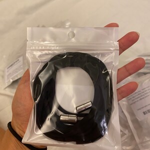 Puede incluir: Un collar de cord&oacute;n negro con dos cierres magn&eacute;ticos plateados en una bolsa de pl&aacute;stico transparente.