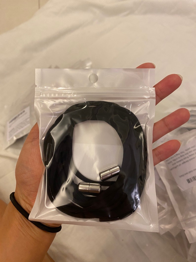 Puede incluir: Un collar de cord&oacute;n negro con dos cierres magn&eacute;ticos plateados en una bolsa de pl&aacute;stico transparente.