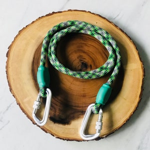 May include: A green and grey rope dog leash with two silver carabiners and green rubber handles.