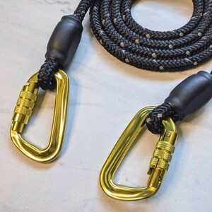 May include: Black rope dog leash with two gold metal clips. The leash is made of thick rope with black and white accents.