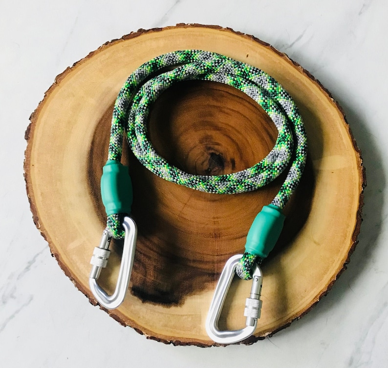 May include: A green and grey rope dog leash with two silver carabiners and green rubber handles.