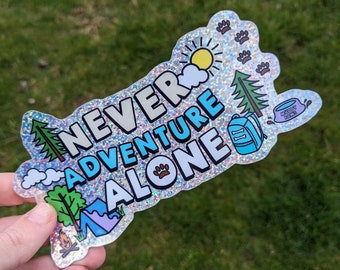May include: A holographic sticker with a sparkly finish. The sticker says "Never Adventure Alone" with a paw print and camping icons.