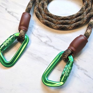 May include: A green and brown rope dog leash with two green metal clips. The leash is made of a thick, durable rope and has a brown leather-like covering on the ends.