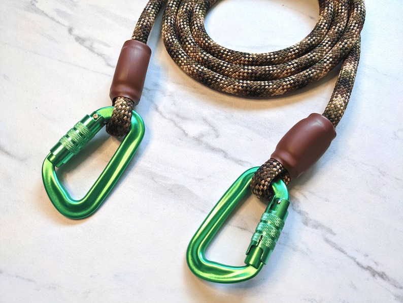 May include: A green and brown rope dog leash with two green metal clips. The leash is made of a thick, durable rope and has a brown leather-like covering on the ends.