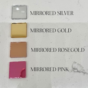 May include: Four square mirrored tiles in silver, gold, rose gold, and pink. Each tile is labeled with its color name in capital letters. The tiles are arranged in a vertical row against a light-colored background.