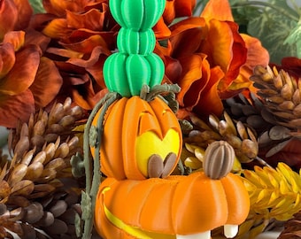 May include: A 3D printed pumpkin-shaped figurine of a cartoon dog with a green pumpkin hat. The figurine is surrounded by fall-colored flowers and pine cones.