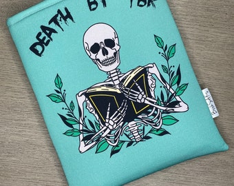 May include: A teal blue book sleeve featuring a skeleton reading a book. The text on the sleeve reads "Death by TBR".