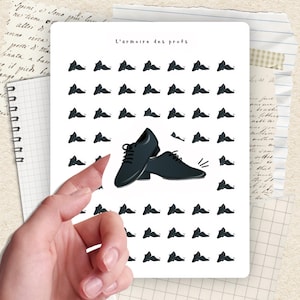 Peut inclure: Un autocollant avec une paire de chaussures de ville noires à lacets, entourée de petites illustrations de chaussures. Le texte "L'armoire des profs" est en haut. L'autocollant est tenu par une main, avec un fond de papier et de notes manuscrites.