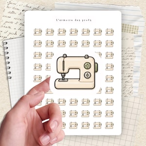 May include: A sticker sheet with a cream-coloured sewing machine illustration, surrounded by smaller sewing machine icons. The text "L'armoire des profs" is at the top. The sticker sheet is held by a hand.