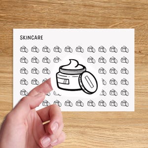 Peut inclure: Une feuille d'autocollants avec une illustration en noir et blanc d'un pot de crème pour le visage. La feuille indique "SKINCARE" en haut.