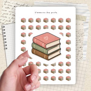 Könnte beinhalten: Ein Stickerbogen mit einem Stapel von drei Büchern, das obere mit einem Herzen, umgeben von kleineren Buchillustrationen. Der Text "L'armoire des profs" steht oben. Der Aufkleber wird von einer Hand vor einem Hintergrund aus liniertem Papier und Schrift gehalten.