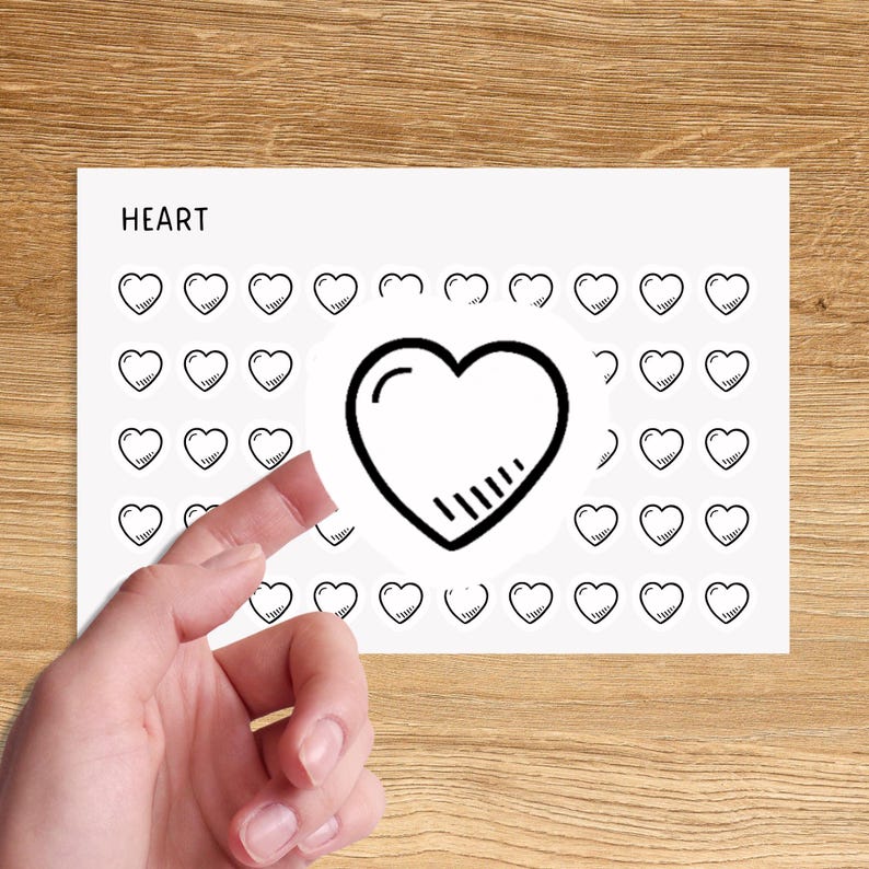 May include: A sheet of white paper with the word "HEART" printed at the top. The paper is covered with small black heart stickers. One large black heart sticker is partially peeled off the sheet.