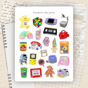 Puede incluir: Una colección de pegatinas coloridas con elementos nostálgicos de los años 90. Incluye un Care Bear, un Cubo de Rubik, una Game Boy, una cinta VHS, un juego de Pac-Man y un muñeco troll. El texto "L'armoire des profs" está en la parte superior.