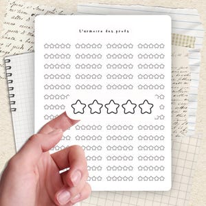 Peut inclure: Une feuille d'autocollants blanche avec le texte "L'armoire des profs" et de nombreux autocollants en forme d'étoile. Une main décolle un autocollant en forme d'étoile. Le fond comprend du papier de cahier et des notes manuscrites.