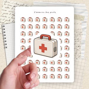 May include: A sheet of stickers featuring a large, white first aid kit with a red cross and handle, surrounded by smaller versions. The text "L'armoire des profs" is at the top. The stickers are on a white background.