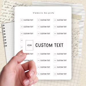 Peut inclure: Une feuille blanche avec le texte "L'armoire des profs" et plusieurs cases avec les mots "CUSTOM TEXT" et des icônes. La feuille est tenue par une main, avec un carnet et d'autres papiers en arrière-plan.
