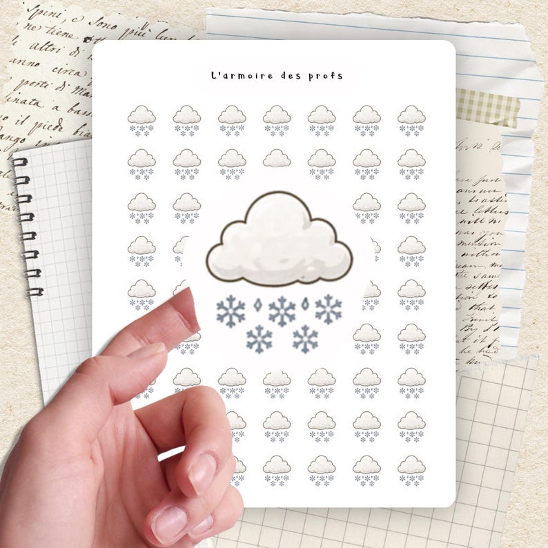 May include: A white sticker sheet with a weather theme. The sheet features illustrations of clouds, snowflakes, and raindrops. The text "L'armoire des profs" is at the top. The sticker sheet is held by a hand.
