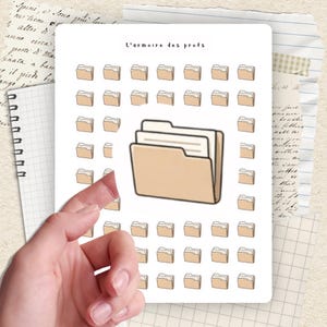 May include: A sheet of stickers featuring beige file folder illustrations. The text "L'armoire des profs" is at the top. The stickers are on a white background, with a hand holding the sheet. The background includes notebook paper and handwritten notes.