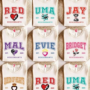 May include: Cream-colored t-shirts with various names in bold, collegiate-style lettering. Each shirt features a graphic and the text "EST. 2025 DESCENDANTS". Names include "RED", "UMA", "JAY", "MAL", "EVIE", "BRIDGET", and "QUEEN OF HEARTS".
