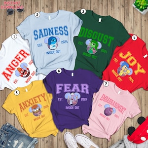 May include: Set of 7 t-shirts featuring characters from the Disney Pixar movie Inside Out. Each shirt has a different character and emotion: Anger, Sadness, Disgust, Joy, Fear, Anxiety, and Embarrassment. The shirts are all white with a colorful graphic print.