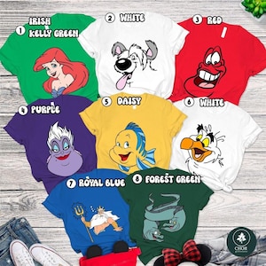 A collection of cartoon character t-shirts, each with a different color and design, laid out on a wooden surface.